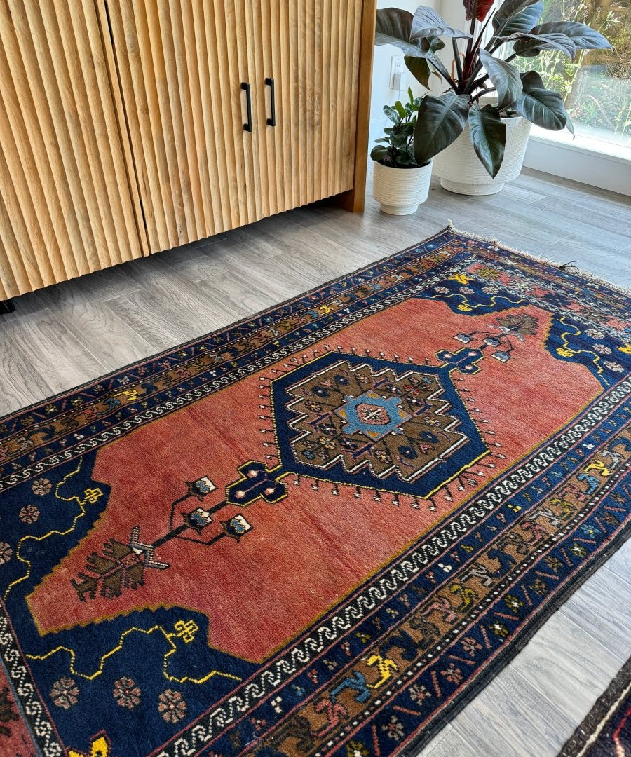 Geometric rug with red center panel, navy border, and multicolor motifs; short fringe edge.