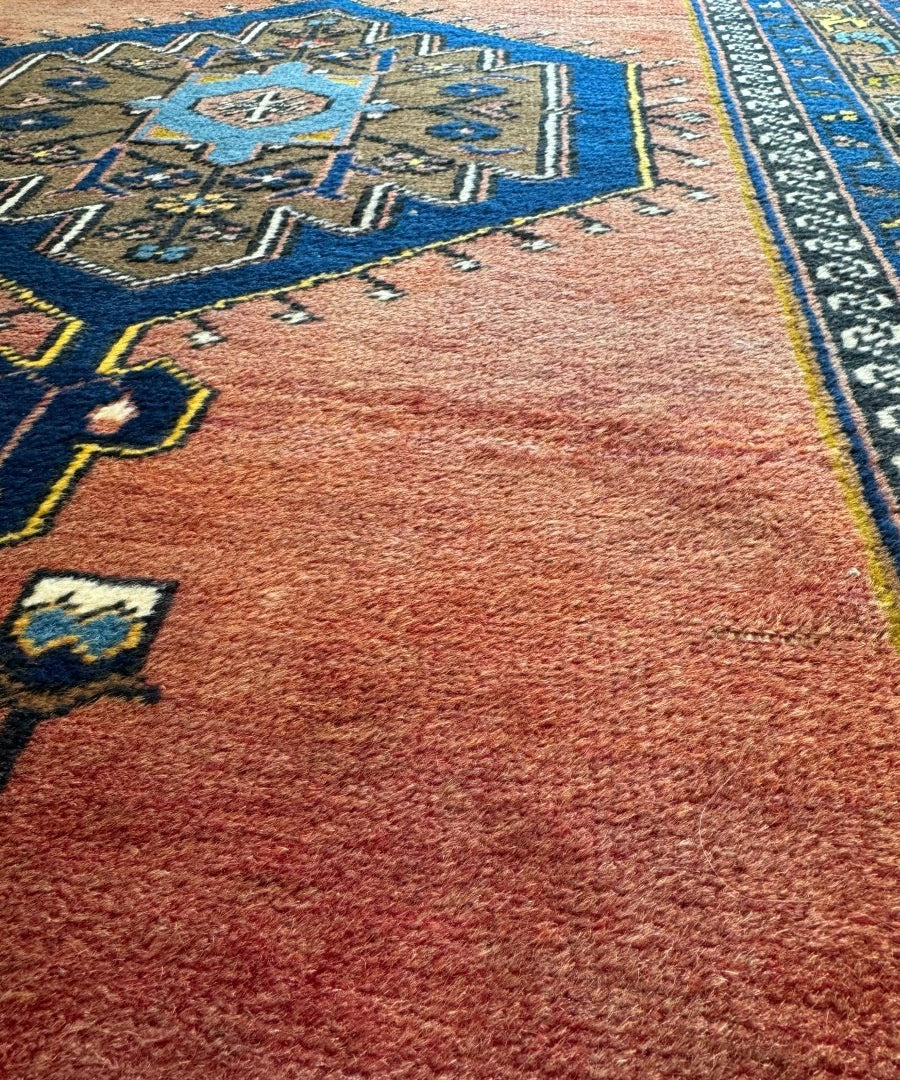 Close-up of red rug pile with blue and teal geometric corner border and small motifs.
