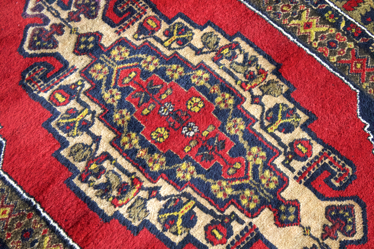 Turkish rug pattern close-up with red ground, navy motifs, and cream geometric border