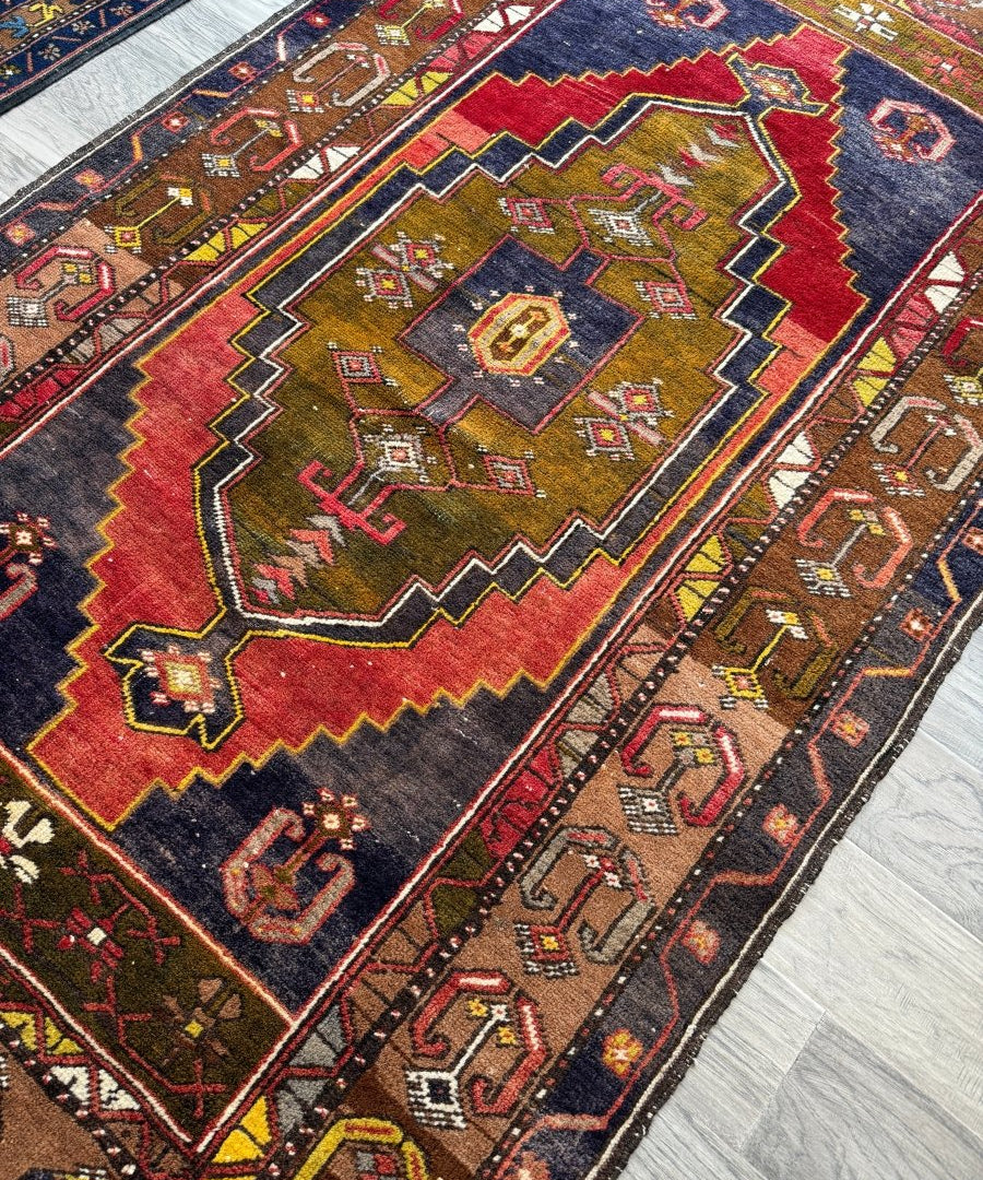 Turkish rug angled view with dark blue center, red and gold chevrons, and small diamond motifs.