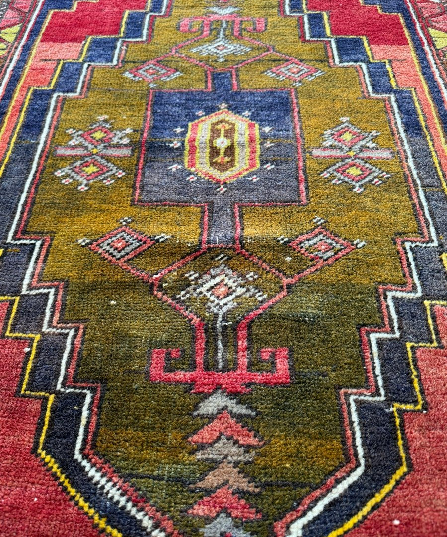 Turkish rug close-up of central cross-like motif in gold and navy with red, green, and pink details.