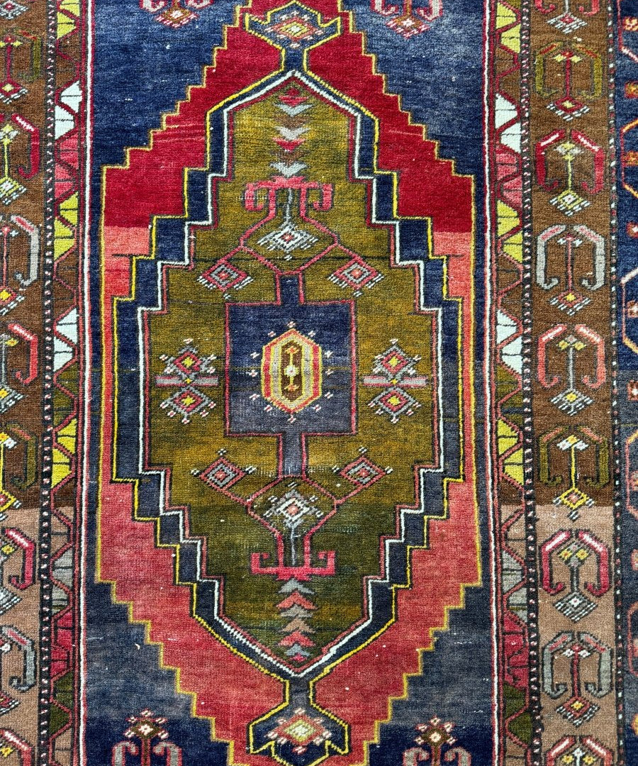 Turkish rug with central medallion, red border, dark blue field, and geometric accents in gold and green.