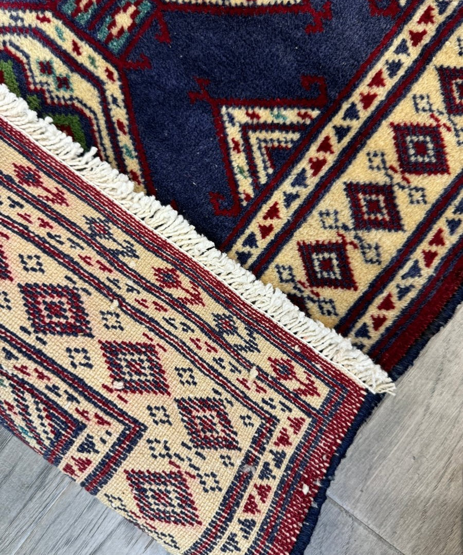 Turkmen mini rug corner border with navy background, cream and red geometric patterns, fringed edge