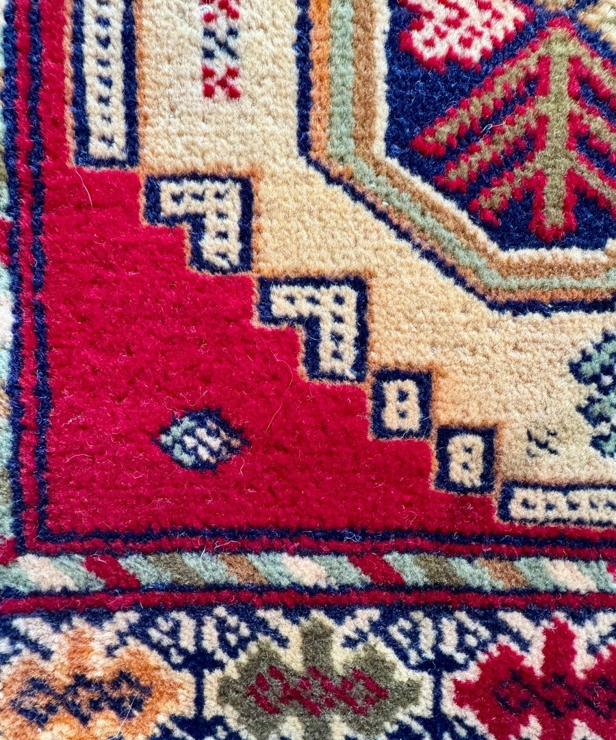 Turkmen mini rug close-up of red, cream, and blue geometric patterns with small square details