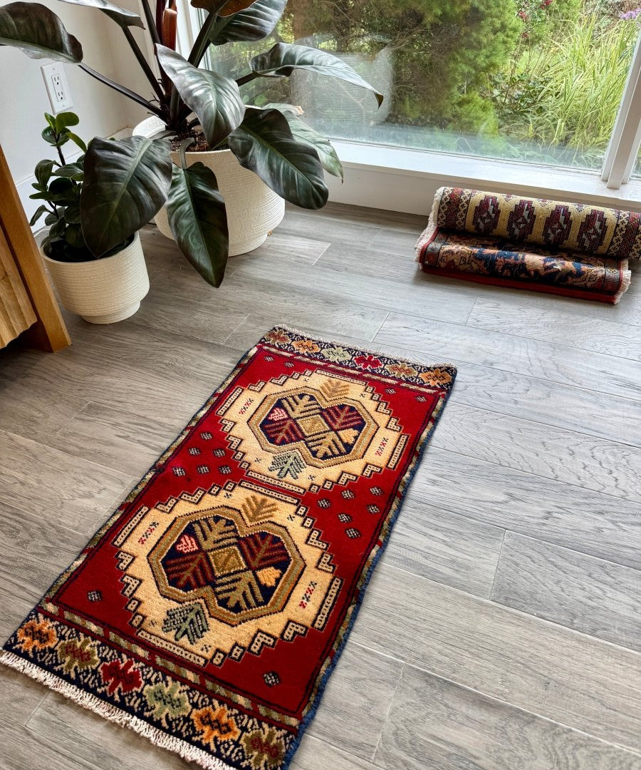 Turkmen mini rug laid on floor, red with cream and blue diamond motifs and dark border