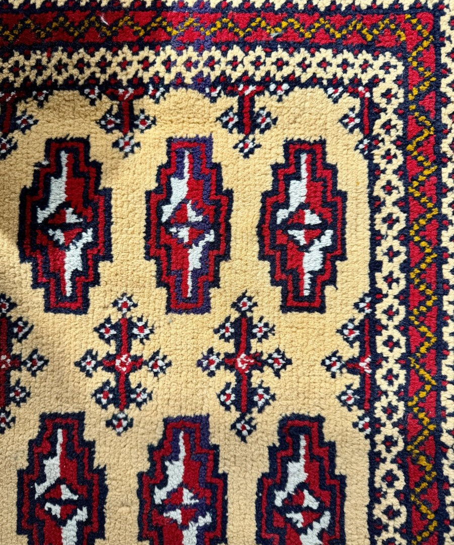 Mini rug close-up with cream weave, dark blue and red medallions, small navy cross motifs
