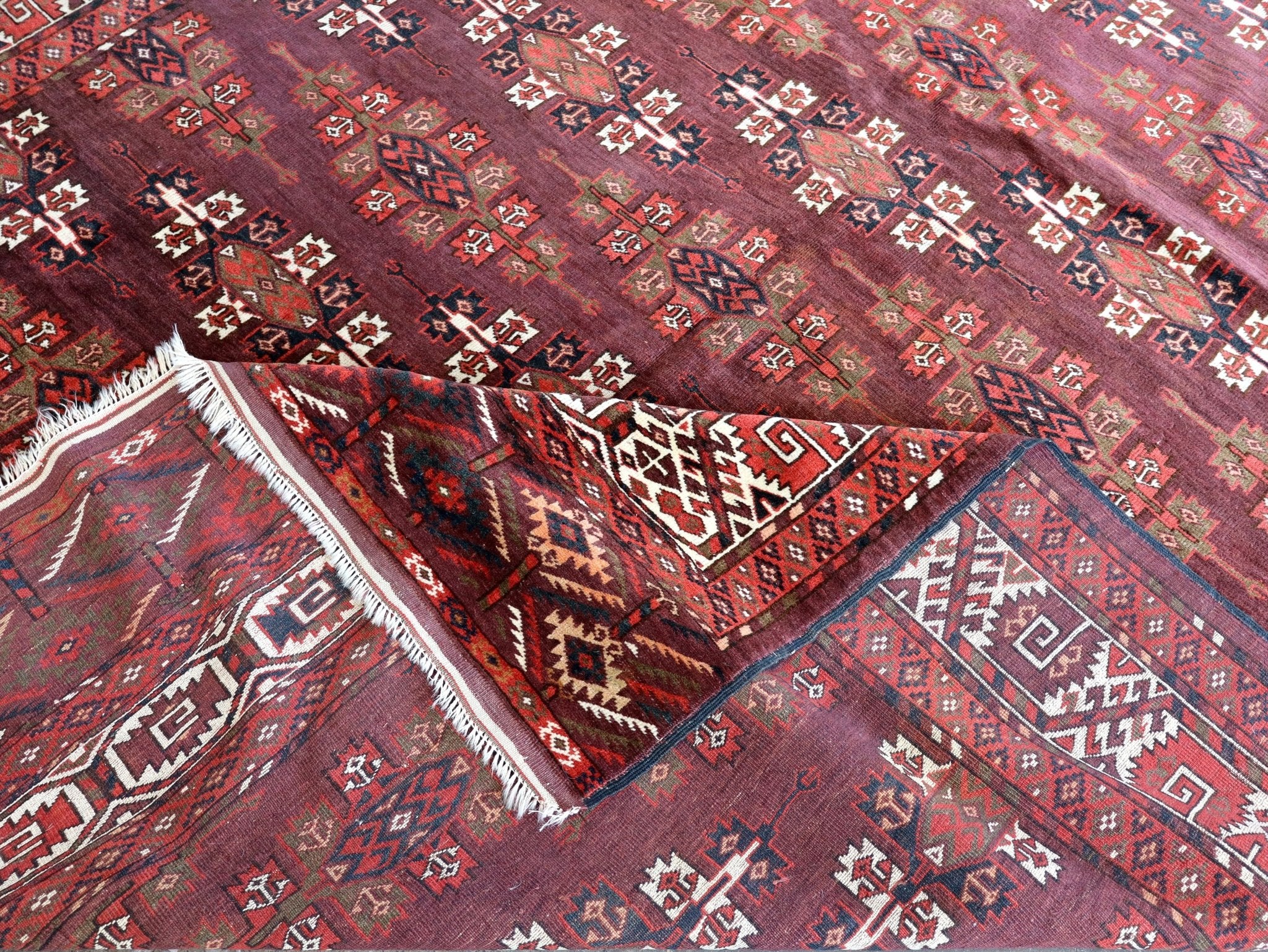 Turkmen Yomut rug with red and navy geometric sections and cream border; fringed corner visible