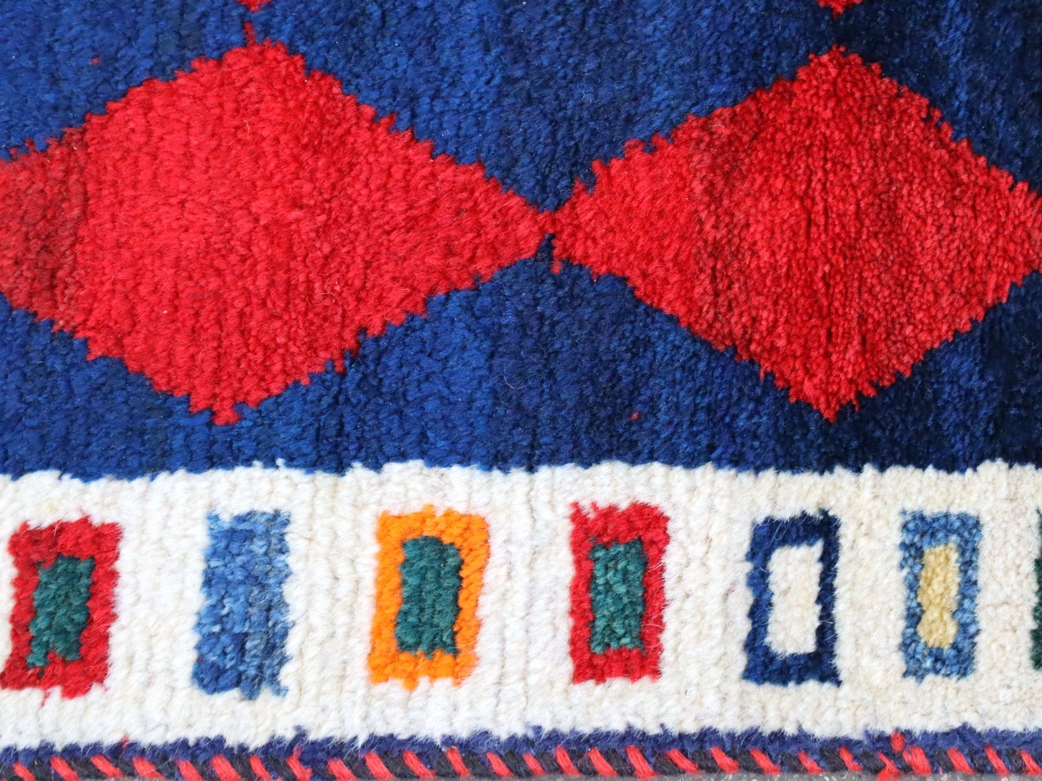 Persian Gabbeh rug edge with red diamond shapes on navy and cream trim