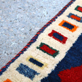 Cream border with multicolor geometric motifs on a navy ground; red accents