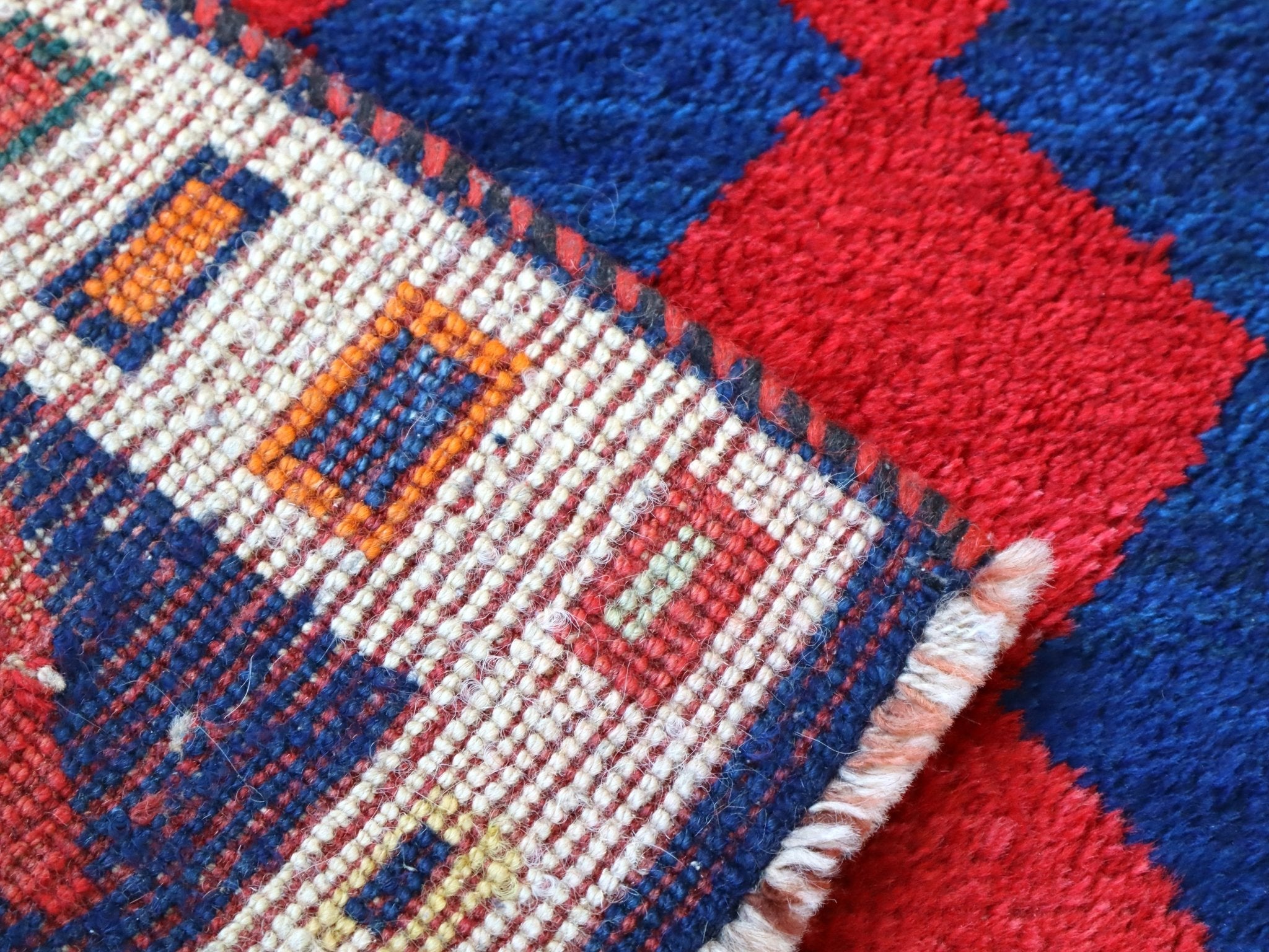 Close-up of cream border weave with multicolor blocks on navy and red diamond rug