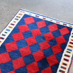 Vintage Persian Gabbeh rug corner with red and navy checker diamonds and cream trim