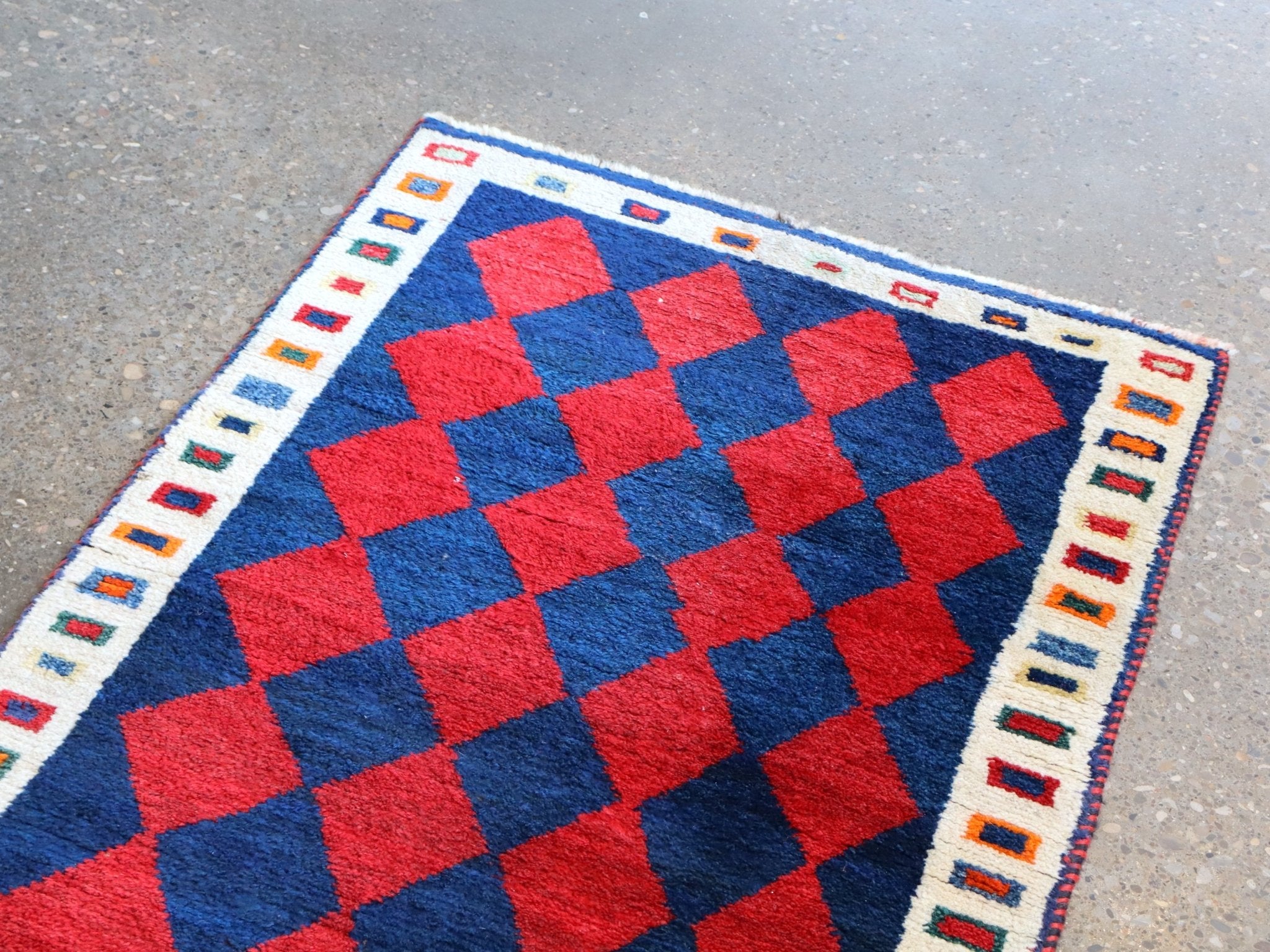 Vintage Persian Gabbeh rug corner with red and navy checker diamonds and cream trim