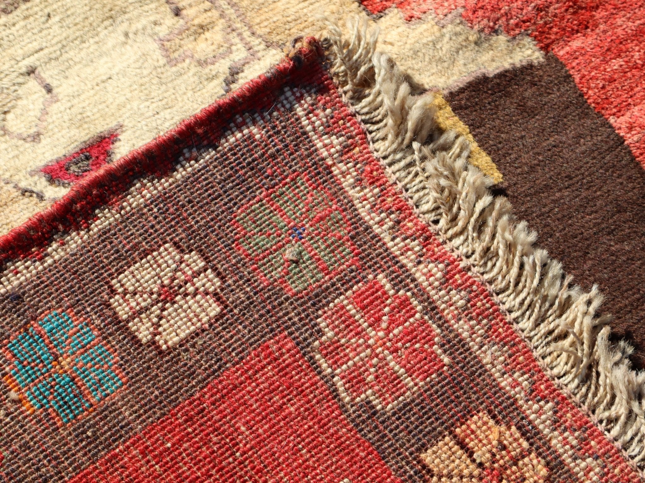 Corner edge of Persian Gabbeh rug with fringe and detailed border weave pattern.