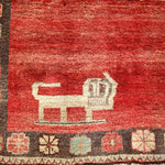 Gabbeh rug close-up with red weave, cream animal motif, and multicolor border blocks