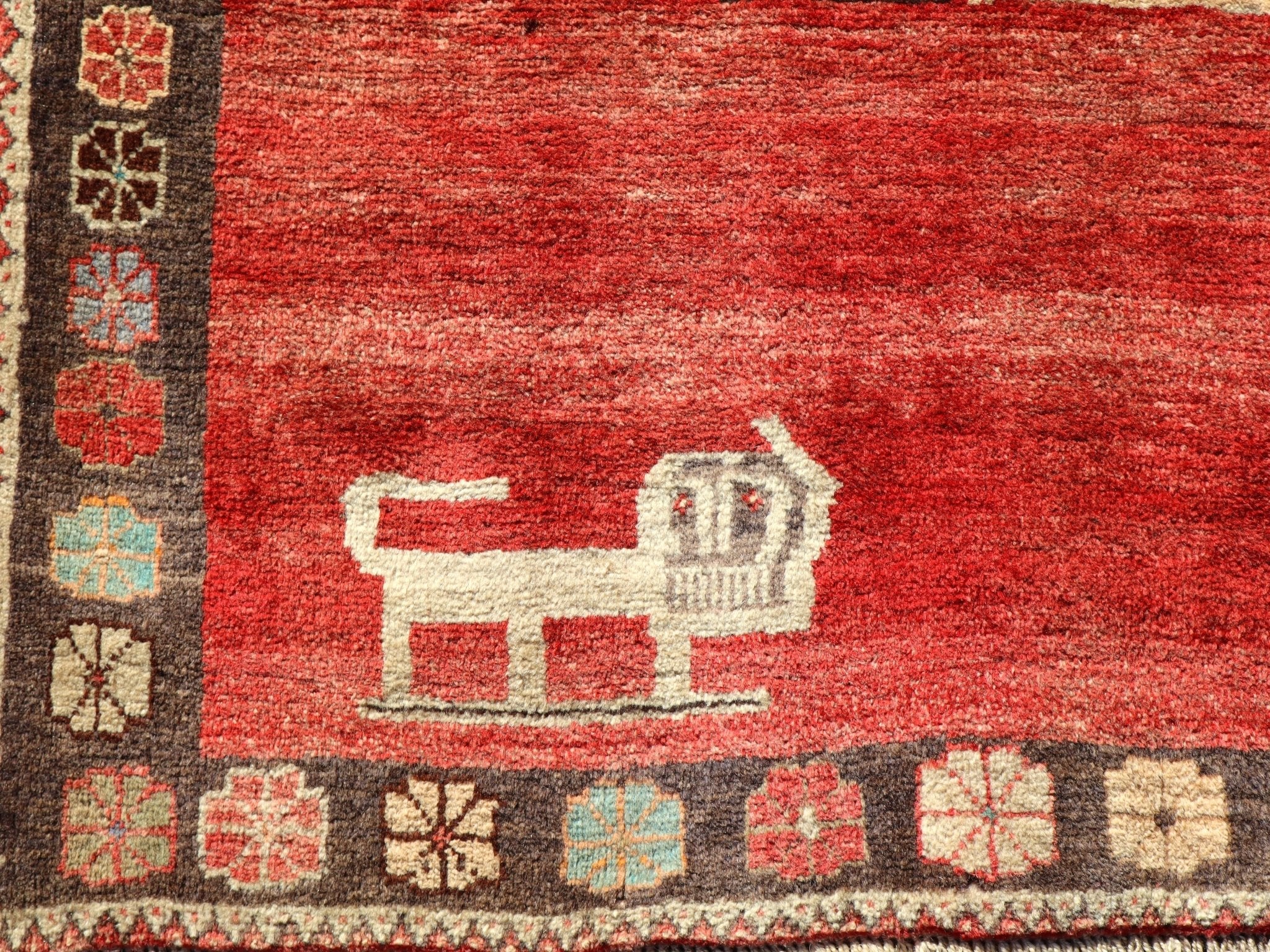 Gabbeh rug close-up with red weave, cream animal motif, and multicolor border blocks