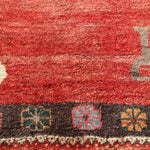 Gabbeh rug close-up texture with red field, dark stripe, and small geometric border symbols