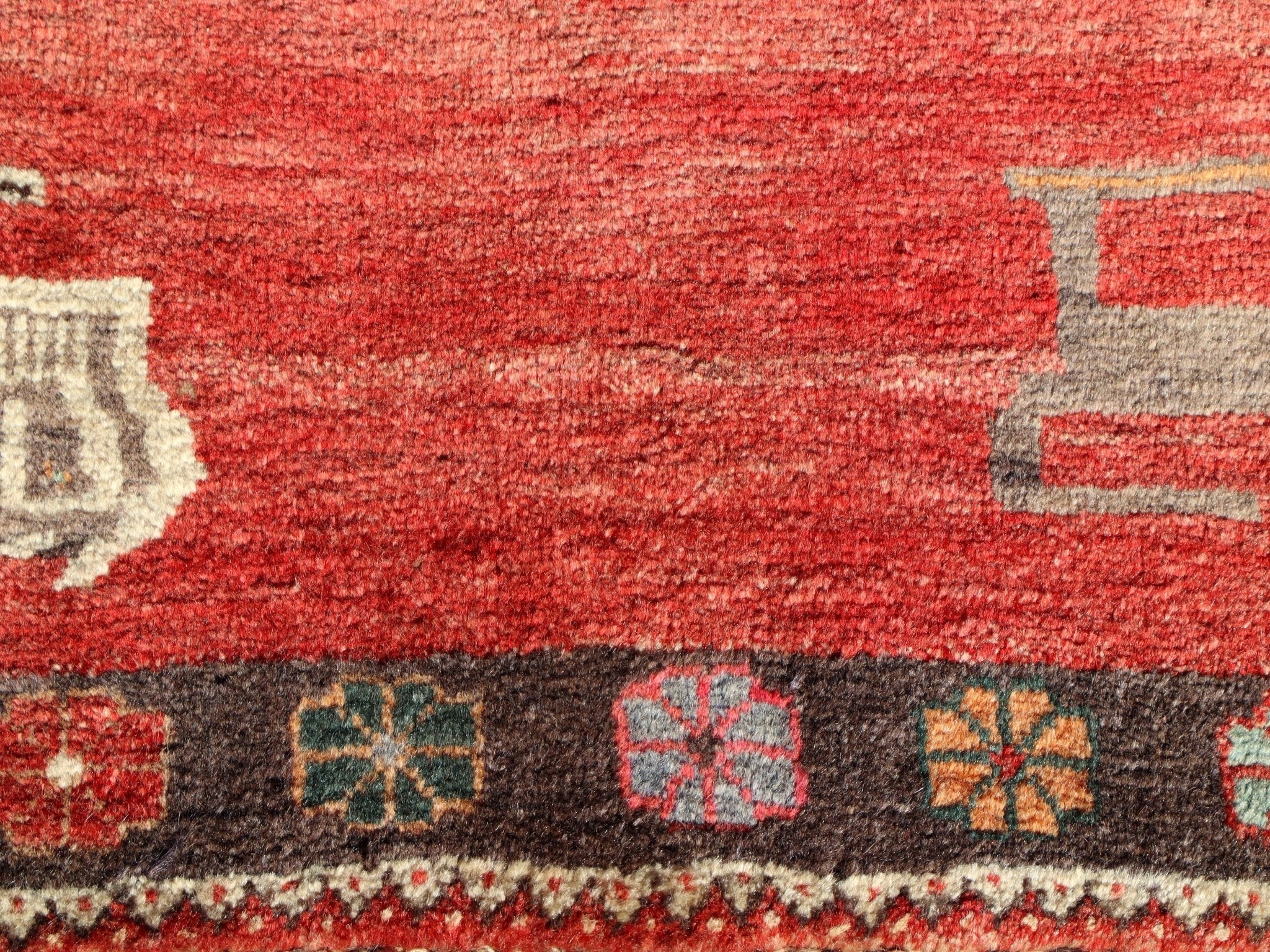 Gabbeh rug close-up texture with red field, dark stripe, and small geometric border symbols