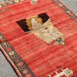 Gabbeh rug angled view with red field, large cream medallion, and dark patterned border