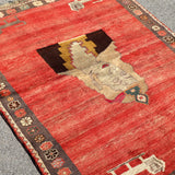 Gabbeh rug angled view with red field, large cream medallion, and dark patterned border