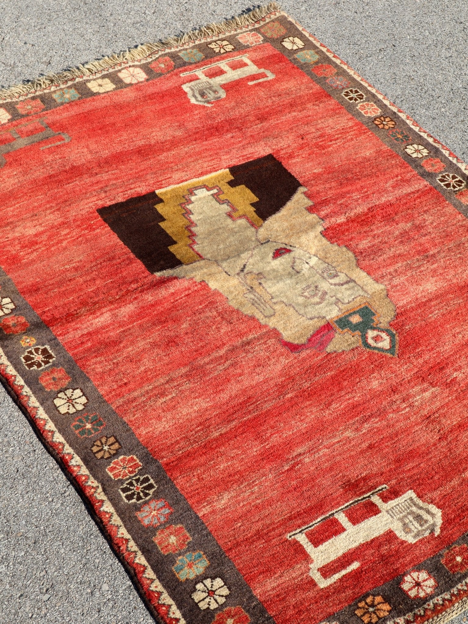 Gabbeh rug angled view with red field, large cream medallion, and dark patterned border