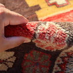Hand holding the edge of a Persian Gabbeh rug, showing thick, textured fringe and weave.