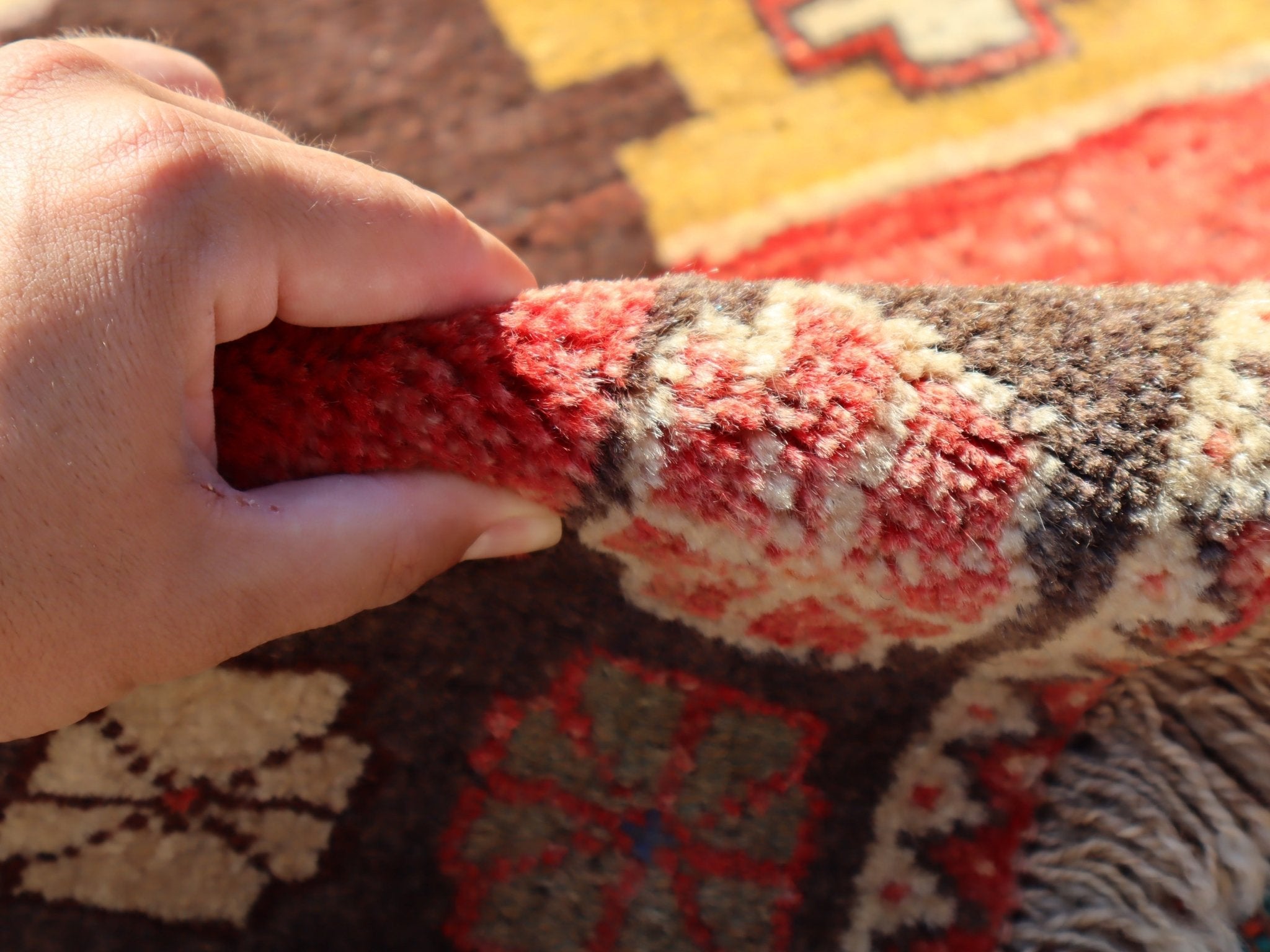 Hand holding the edge of a Persian Gabbeh rug, showing thick, textured fringe and weave.