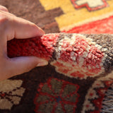 Hand holding the edge of a Persian Gabbeh rug, showing thick, textured fringe and weave.