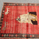 Gabbeh rug top view with red field, large cream animal medallion, and dark decorative border