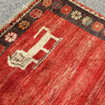 Close-up of red Persian Gabbeh rug with cream abstract medallion and dark border.