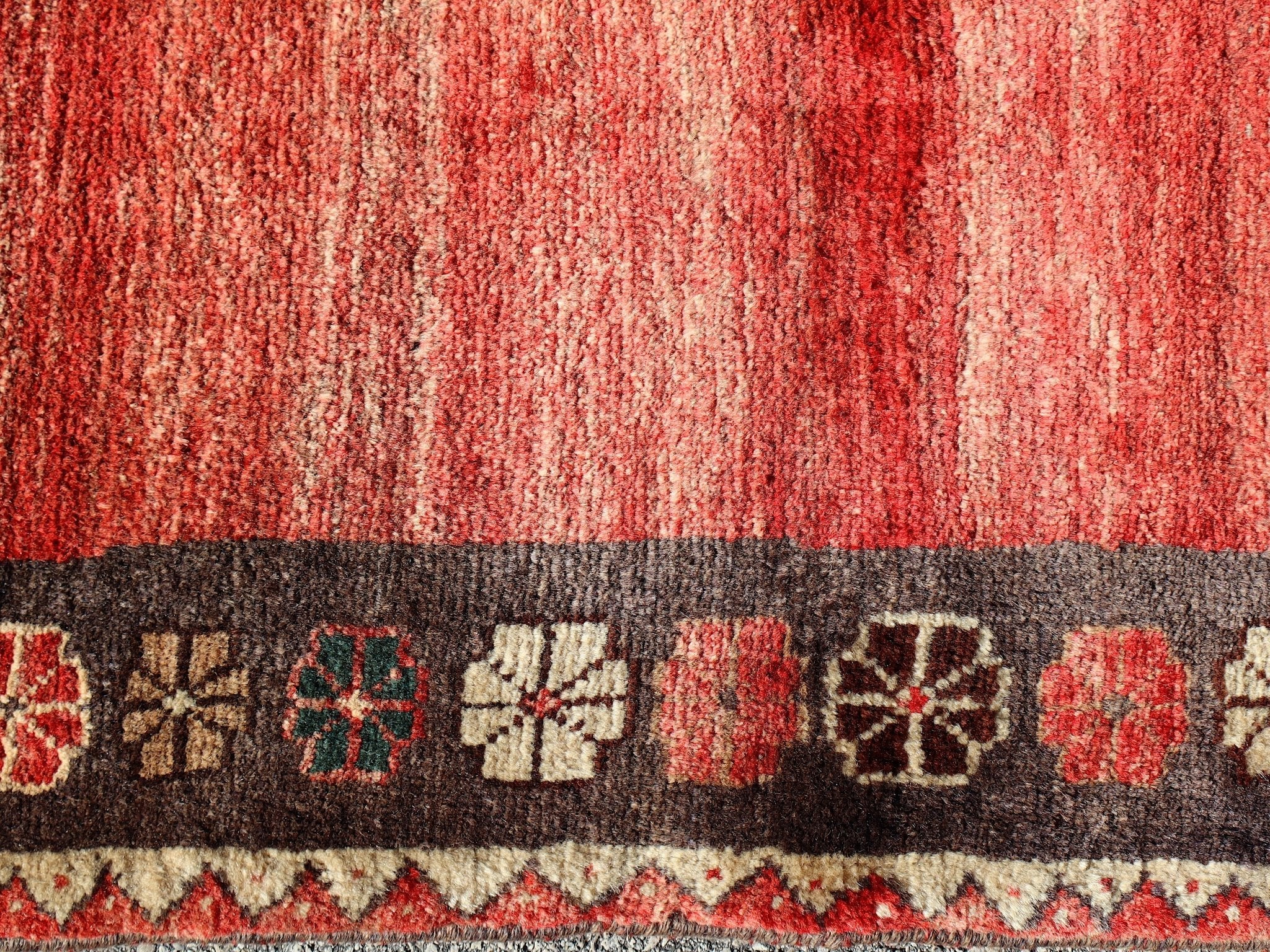Gabbeh rug close-up with red field, cream highlights, and dark geometric border motifs