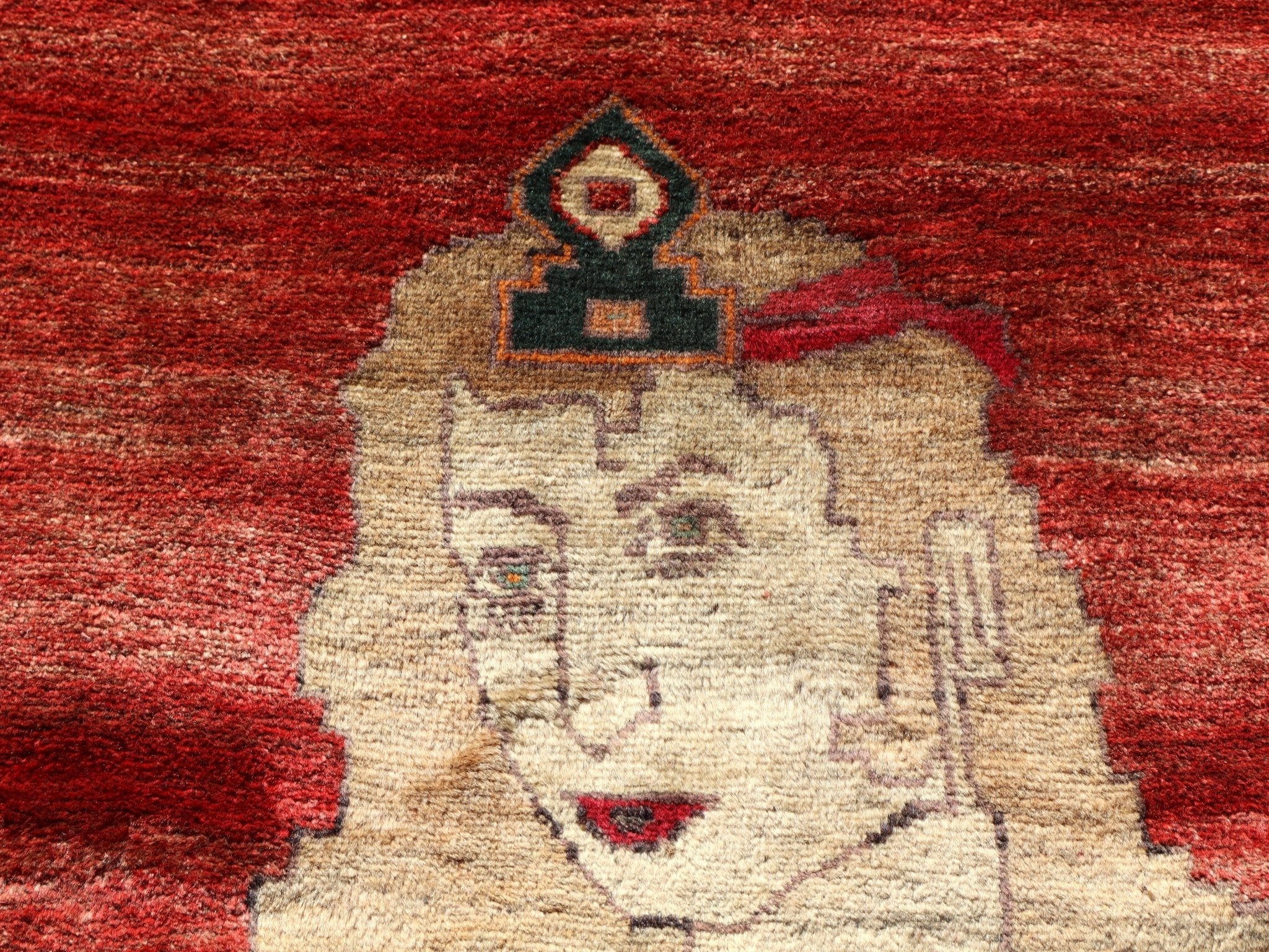 Gabbeh rug close-up showing a cream animal figure on a red background with dark accents