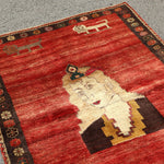 Persian Gabbeh rug with red background, cream figure, dark robe, and patterned border.