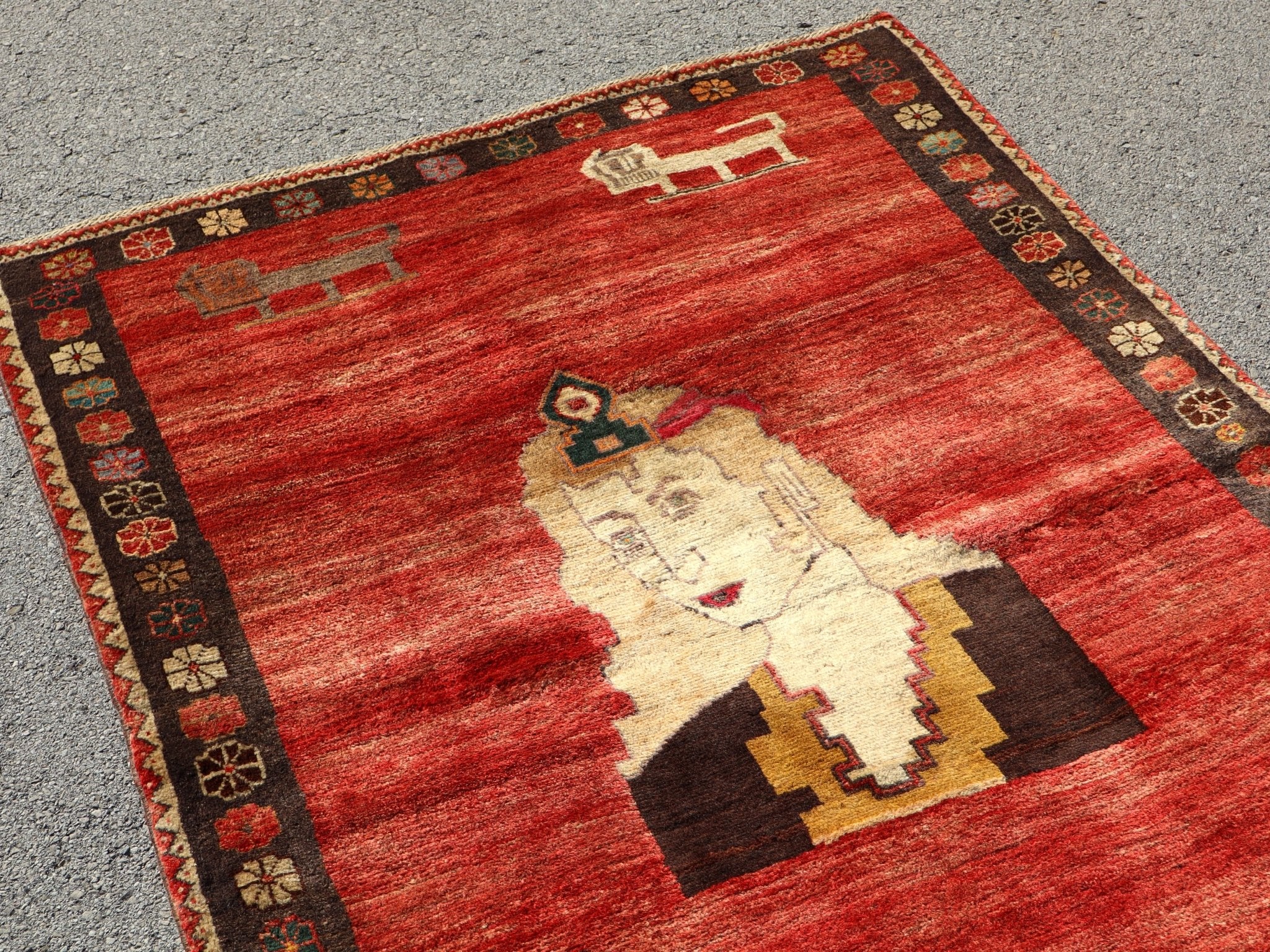 Persian Gabbeh rug with red background, cream figure, dark robe, and patterned border.