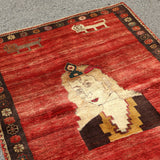 Persian Gabbeh rug with red background, cream figure, dark robe, and patterned border.