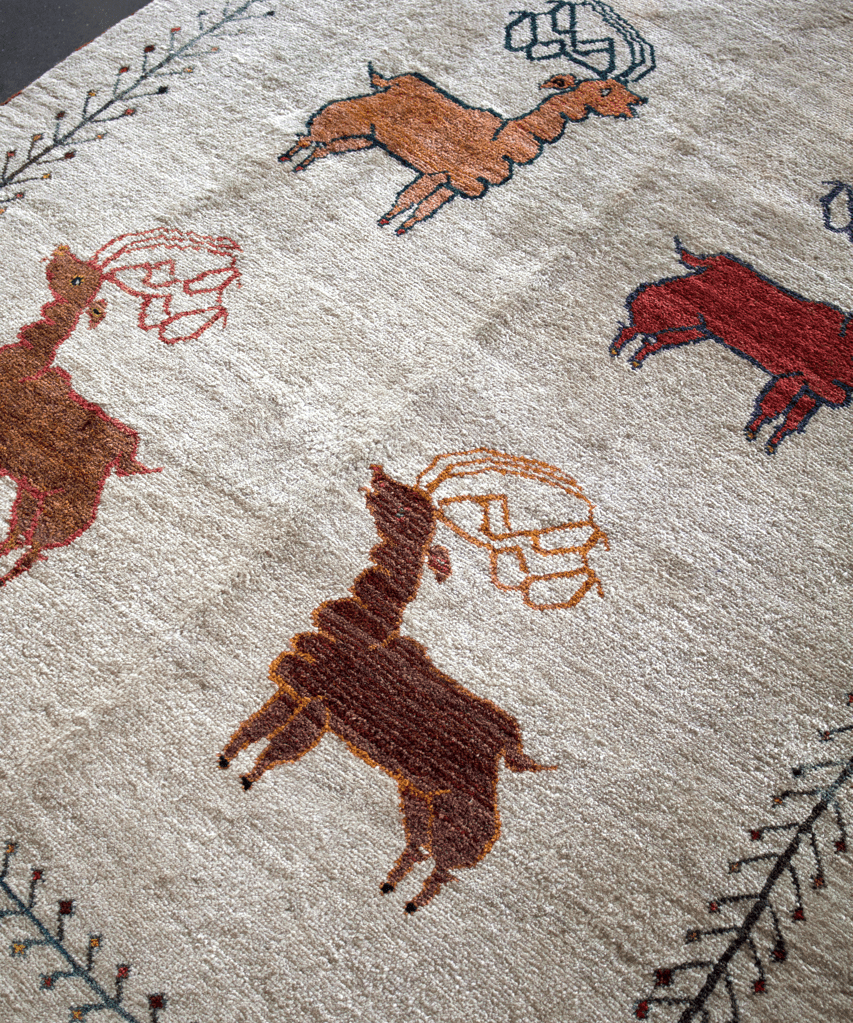 Ivory gabbeh rug with scattered animal motifs in red, brown, and black, stitched border.