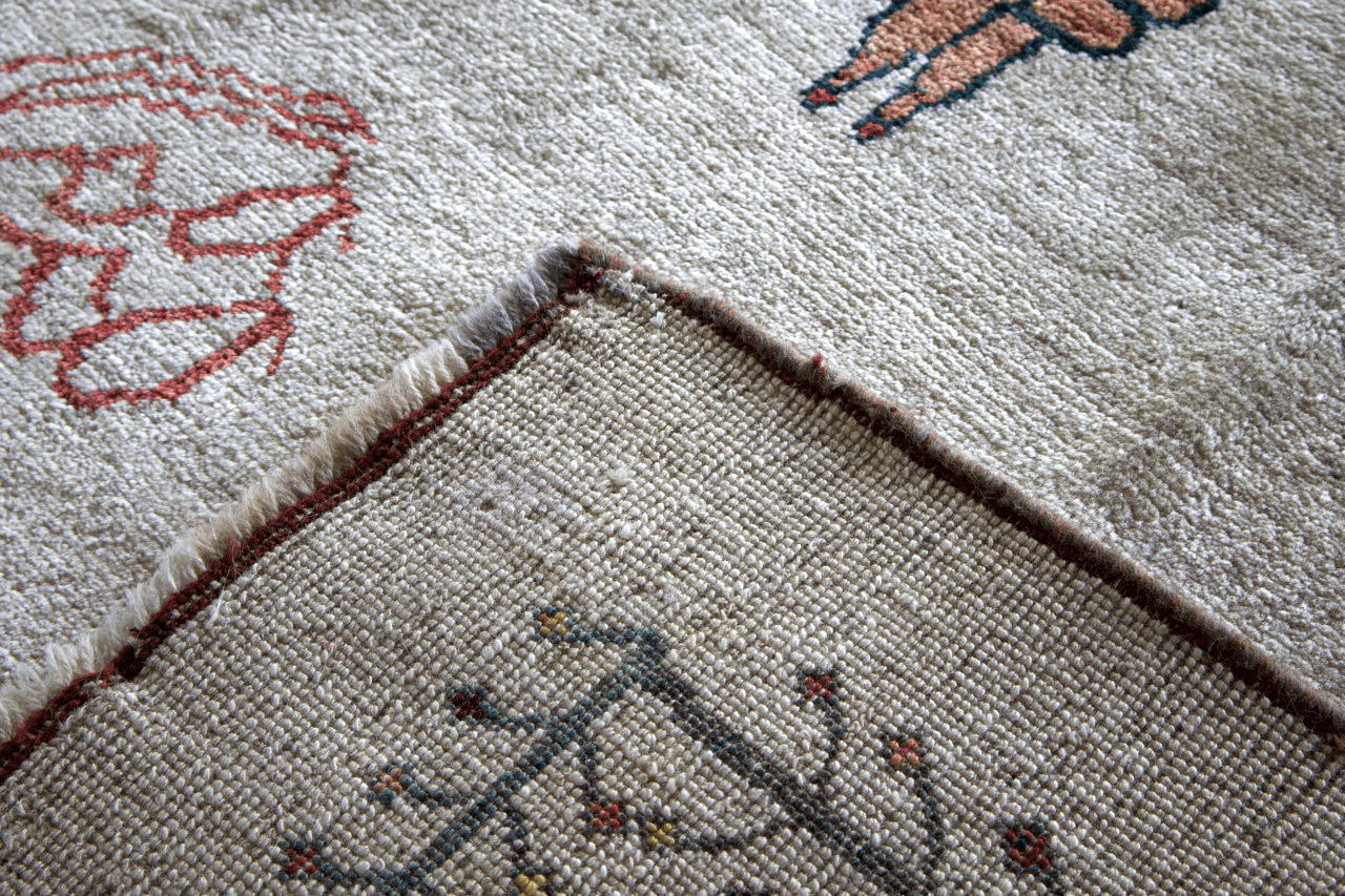 Gabbeh rug corner detail in ivory with dark and blue stitched edging and animal pattern.