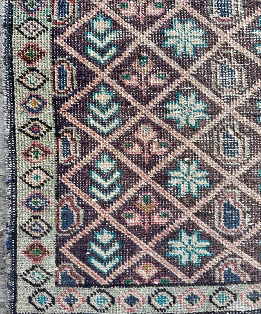 Close-up of vintage rug with detailed diamond motifs in teal, beige, and dark brown