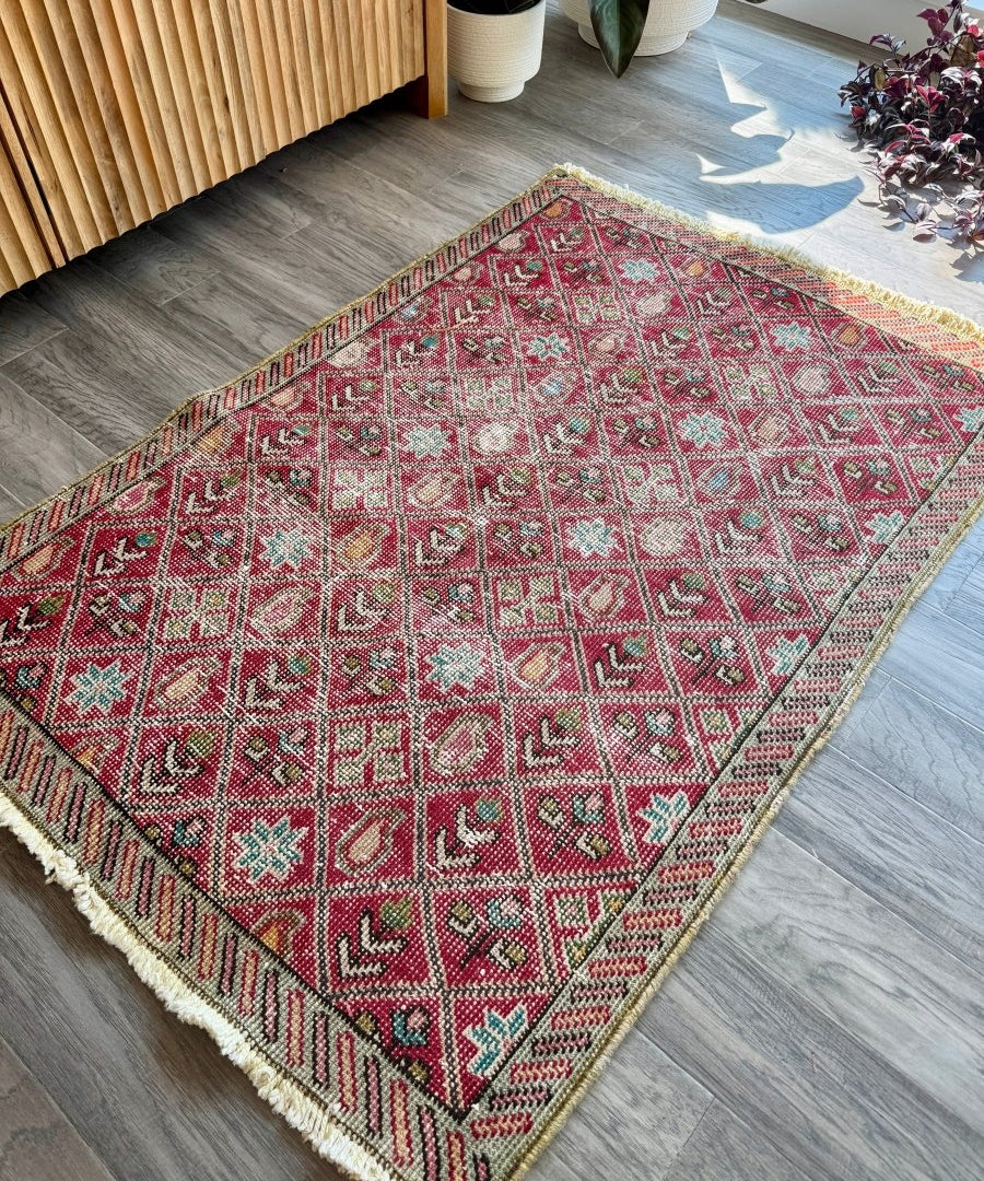 Red patterned vintage rug with diamond motifs, cream accents, and fringe border