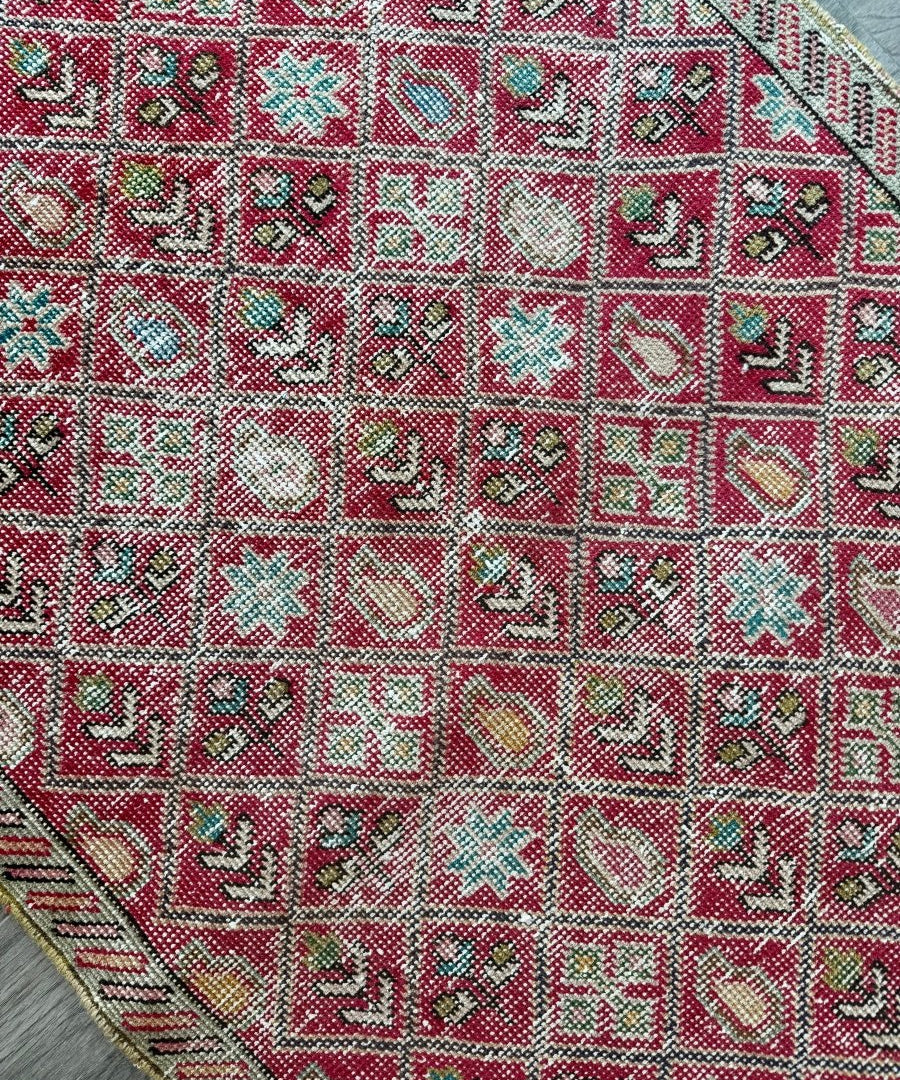 Geometric rug surface in red with cream, teal, and black motif details