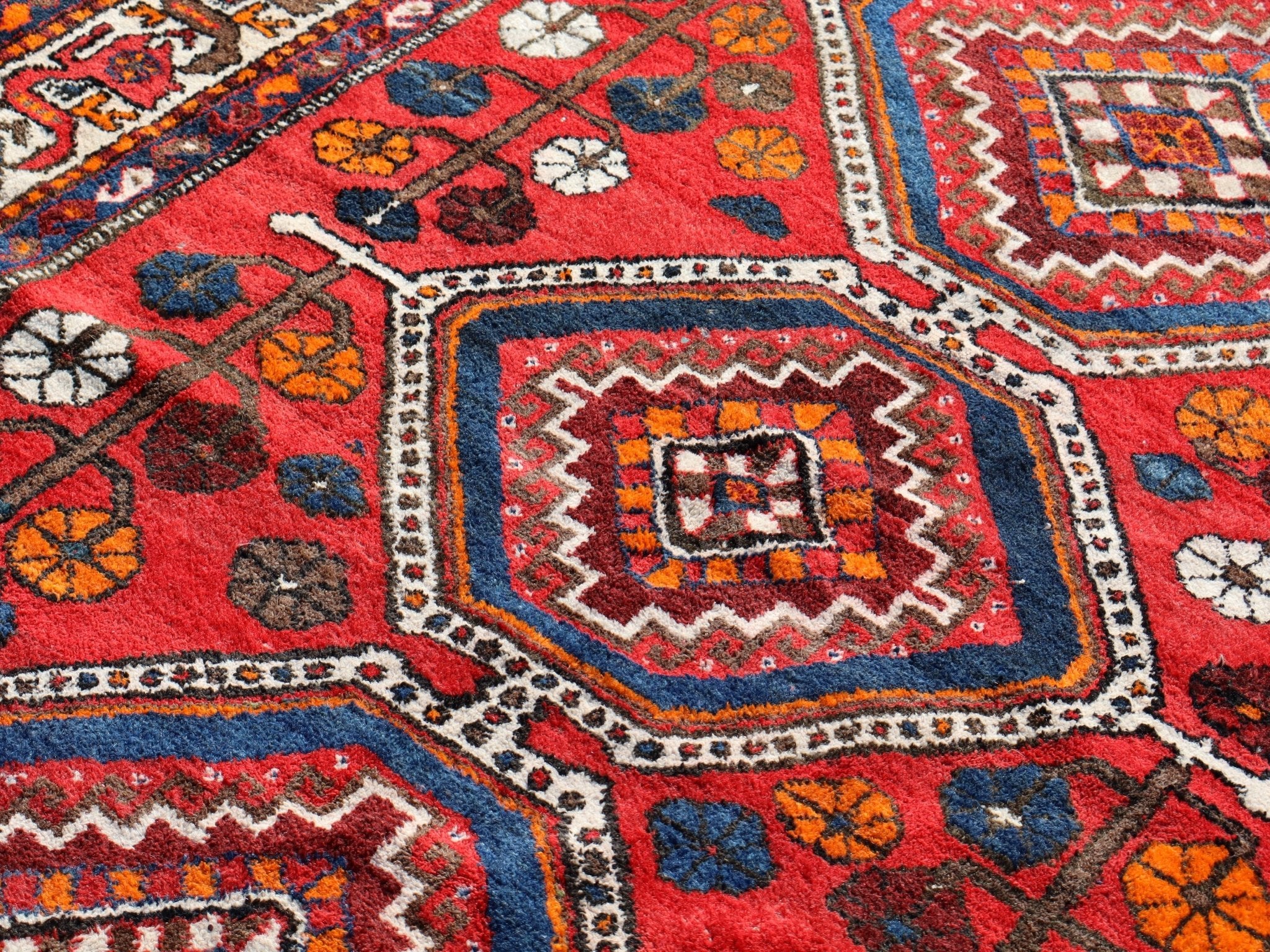 Qashqai rug close-up with red field, central square motif, and blue-and-cream framing