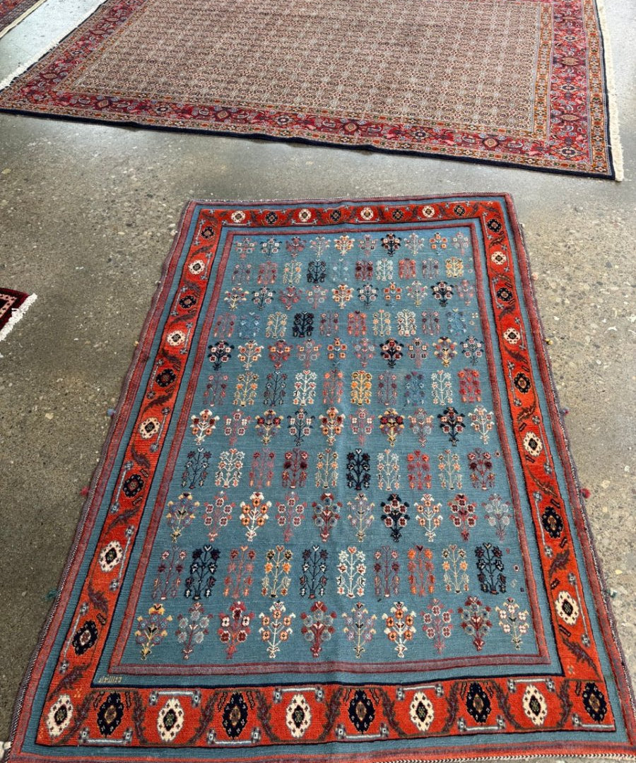 Blue Gabbeh-style kilim rug with red border, small floral patterns, and corner medallions
