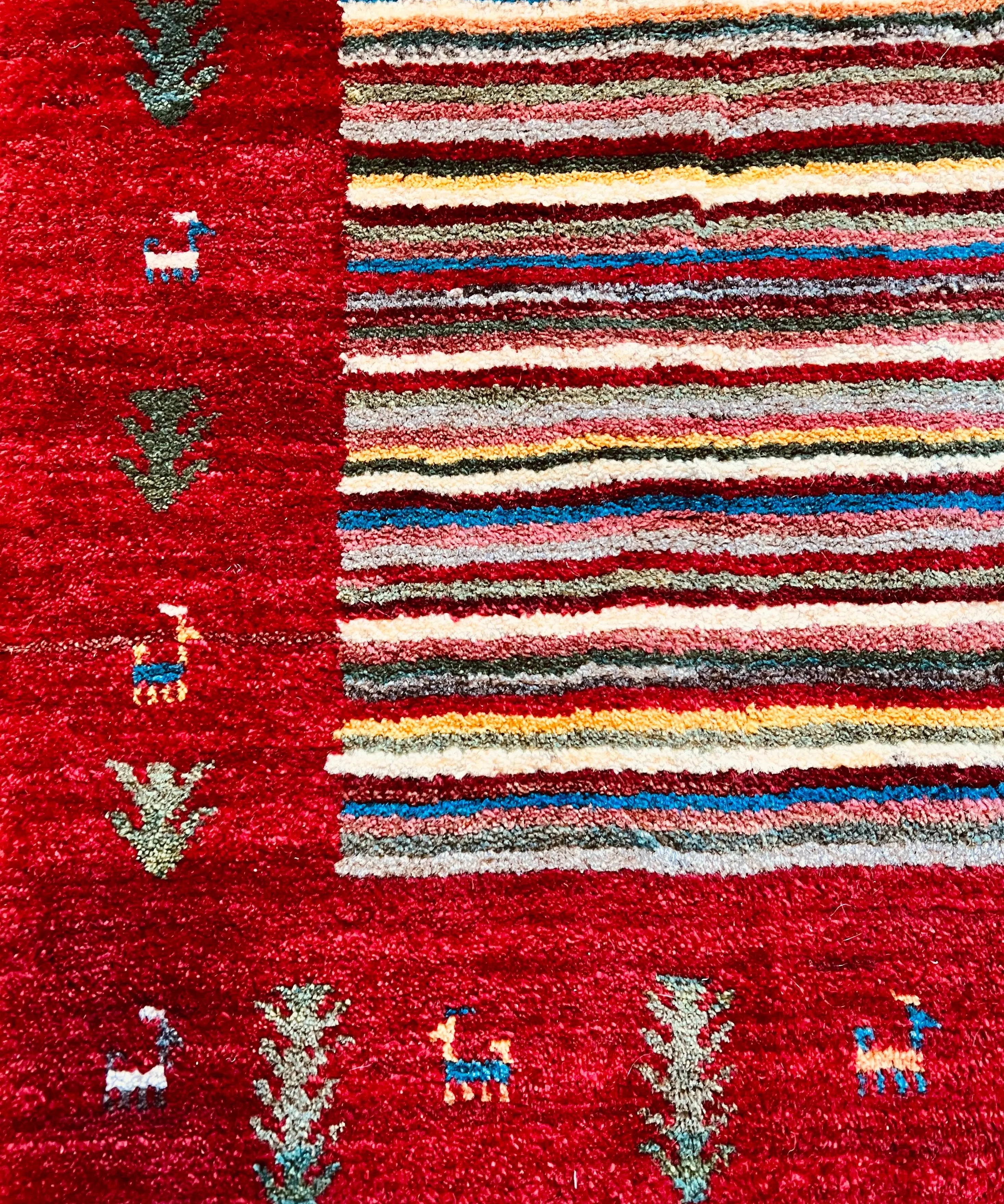 Gabbeh rug with deep red field, multicolor horizontal stripes, and small geometric motifs