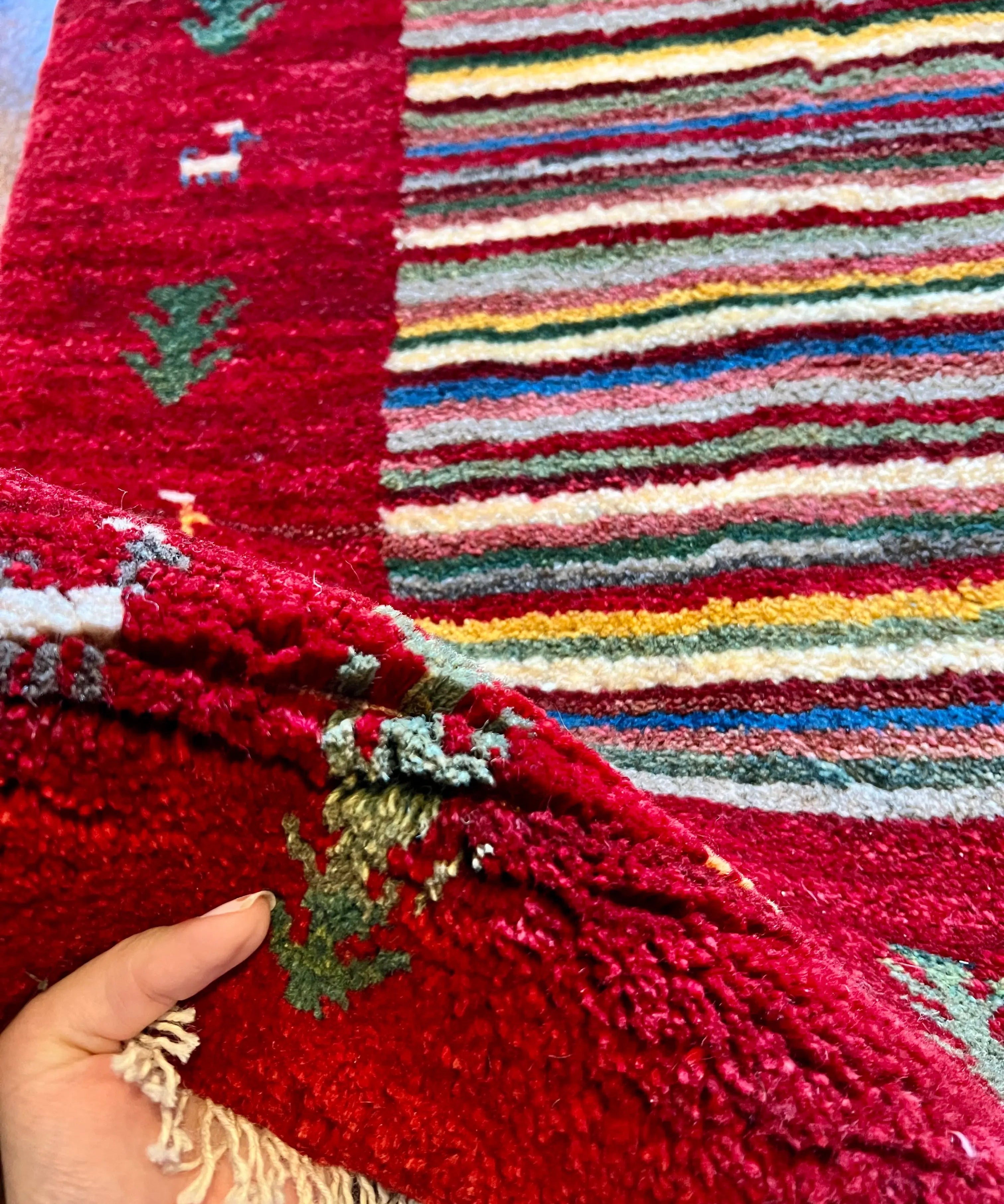 Gabbeh rug corner close-up: deep red pile, small accents, and light fringe with hand