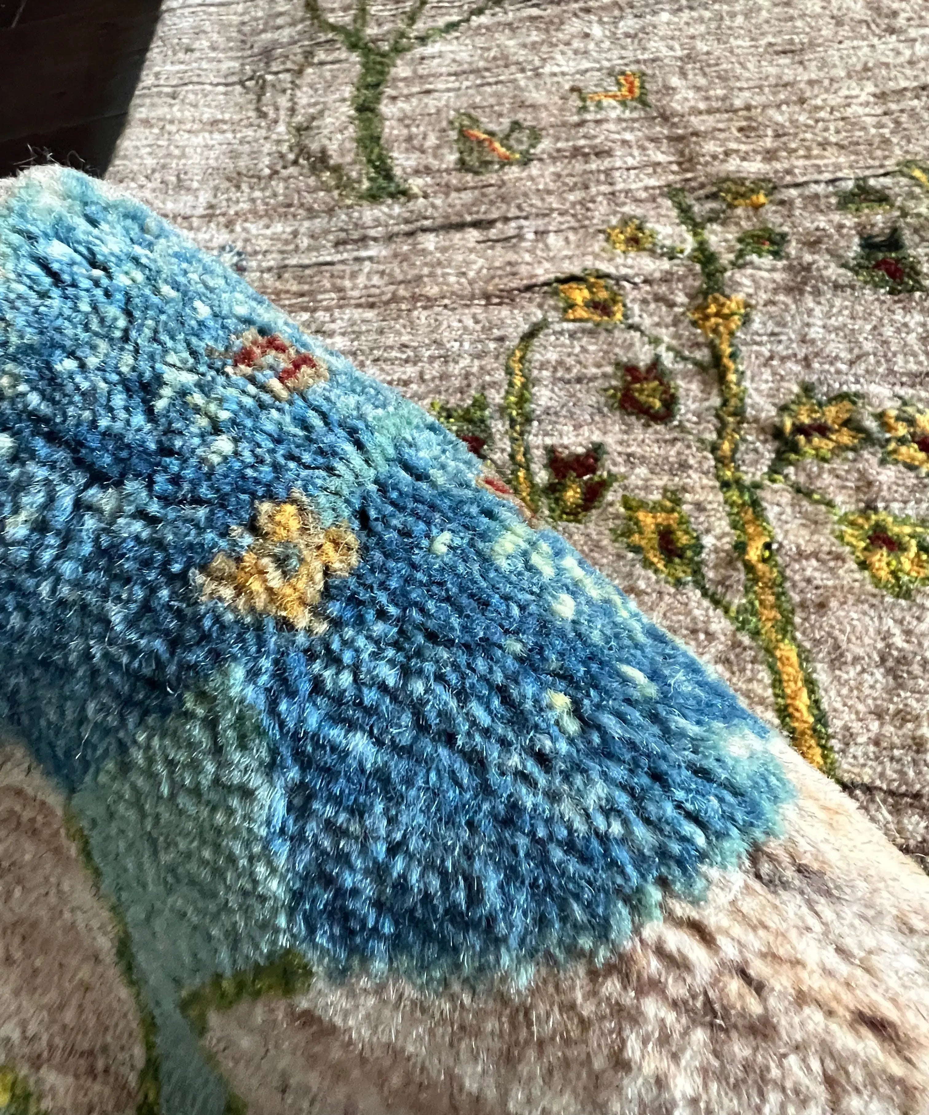 Rug pile close-up with blue shag edge and multicolor vine motif on light backing