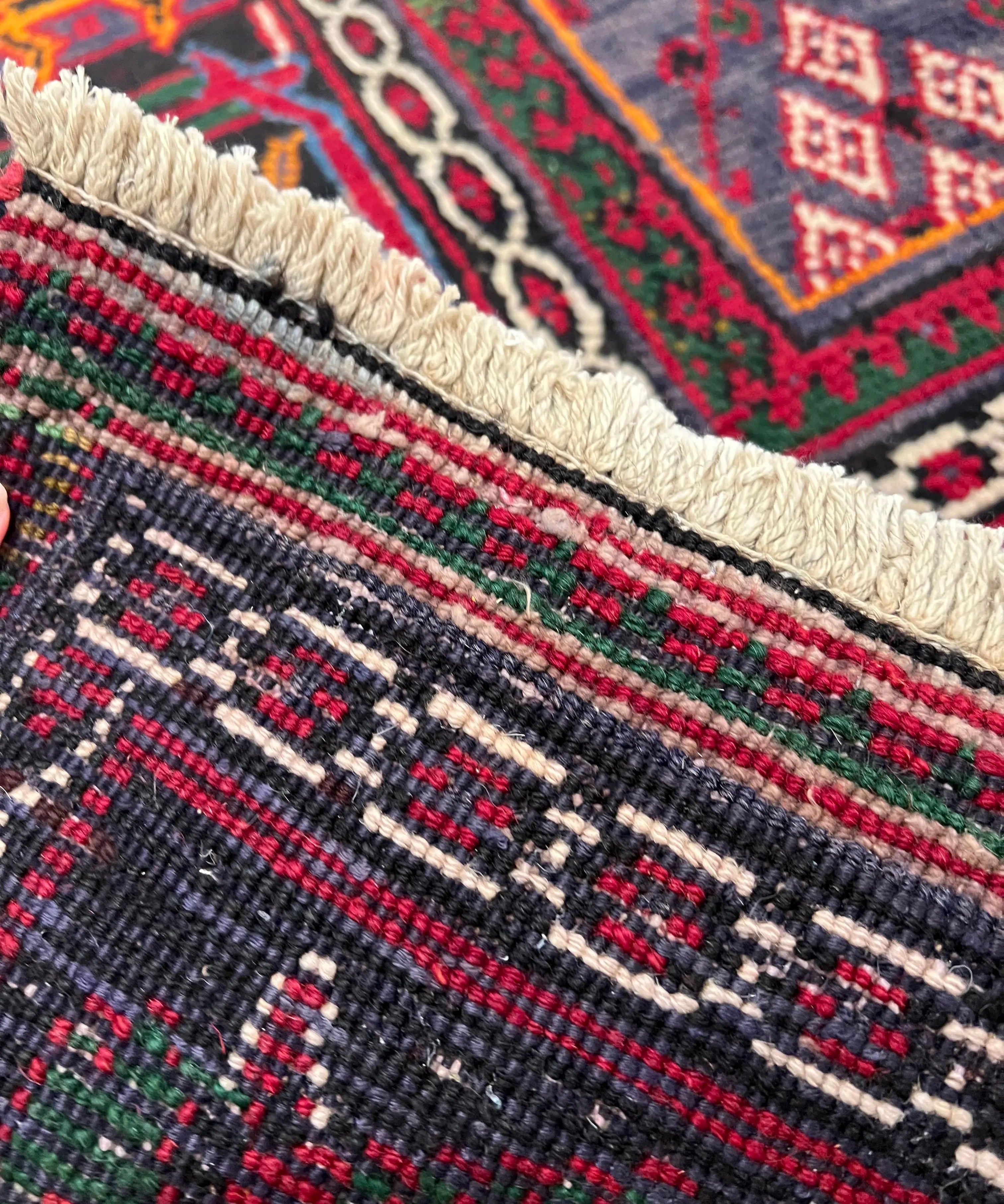 Rug border close-up with cream fringe and red, green, black geometric motifs