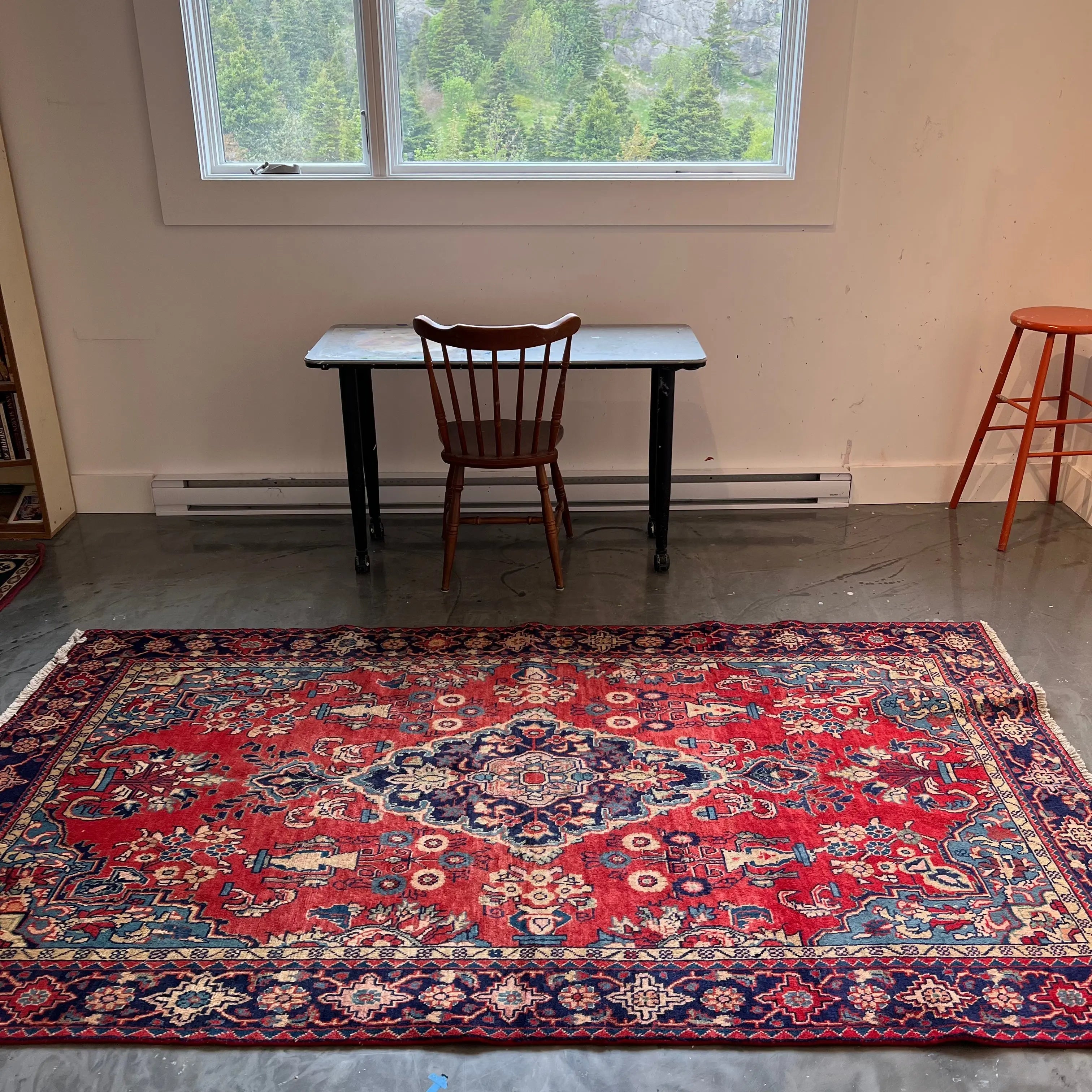 Red Persian-style rug with ornate medallion and navy border, full view on floor.