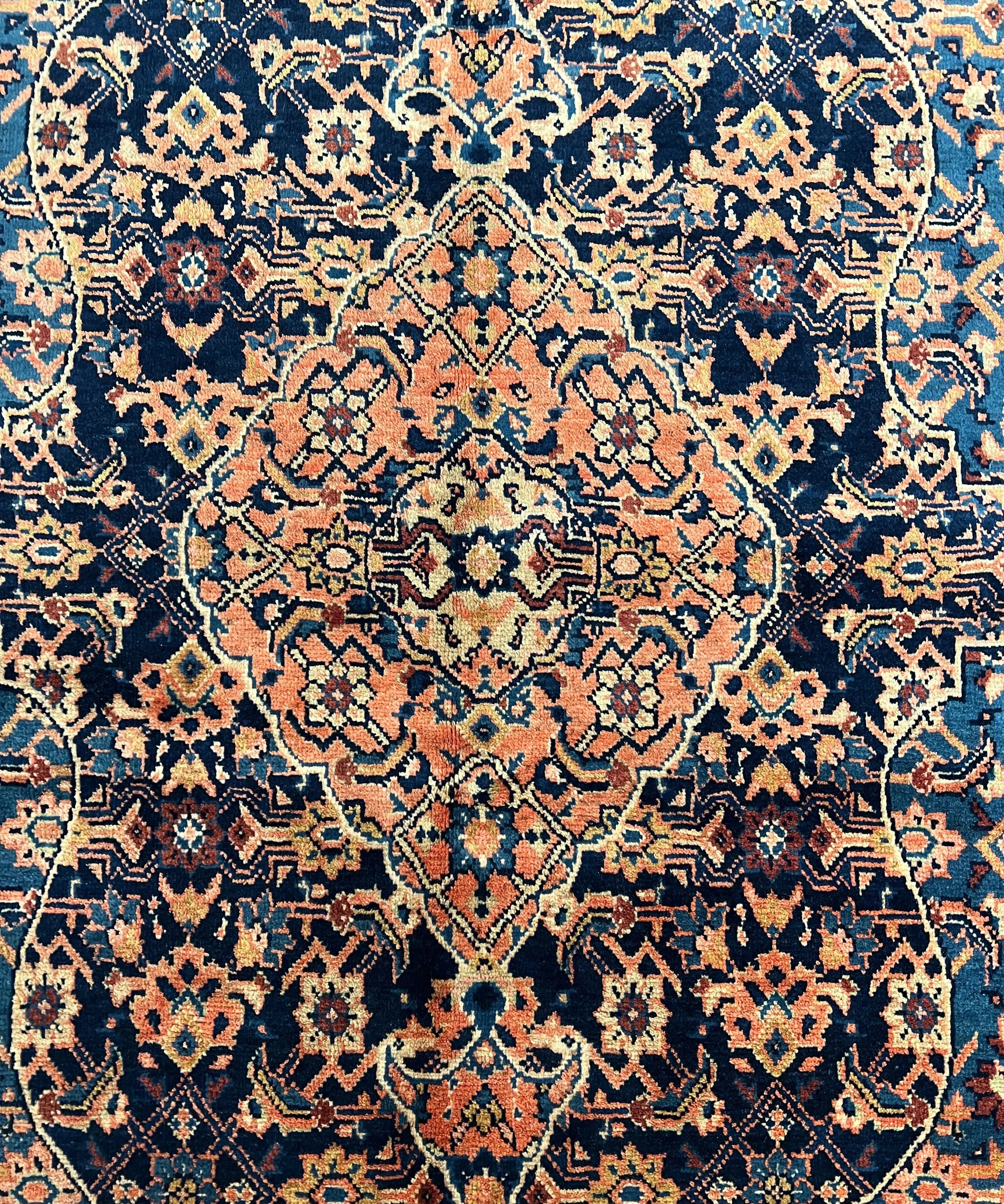 Close-up Persian-style rug pattern in navy, cream, rust, and teal with geometric motifs.
