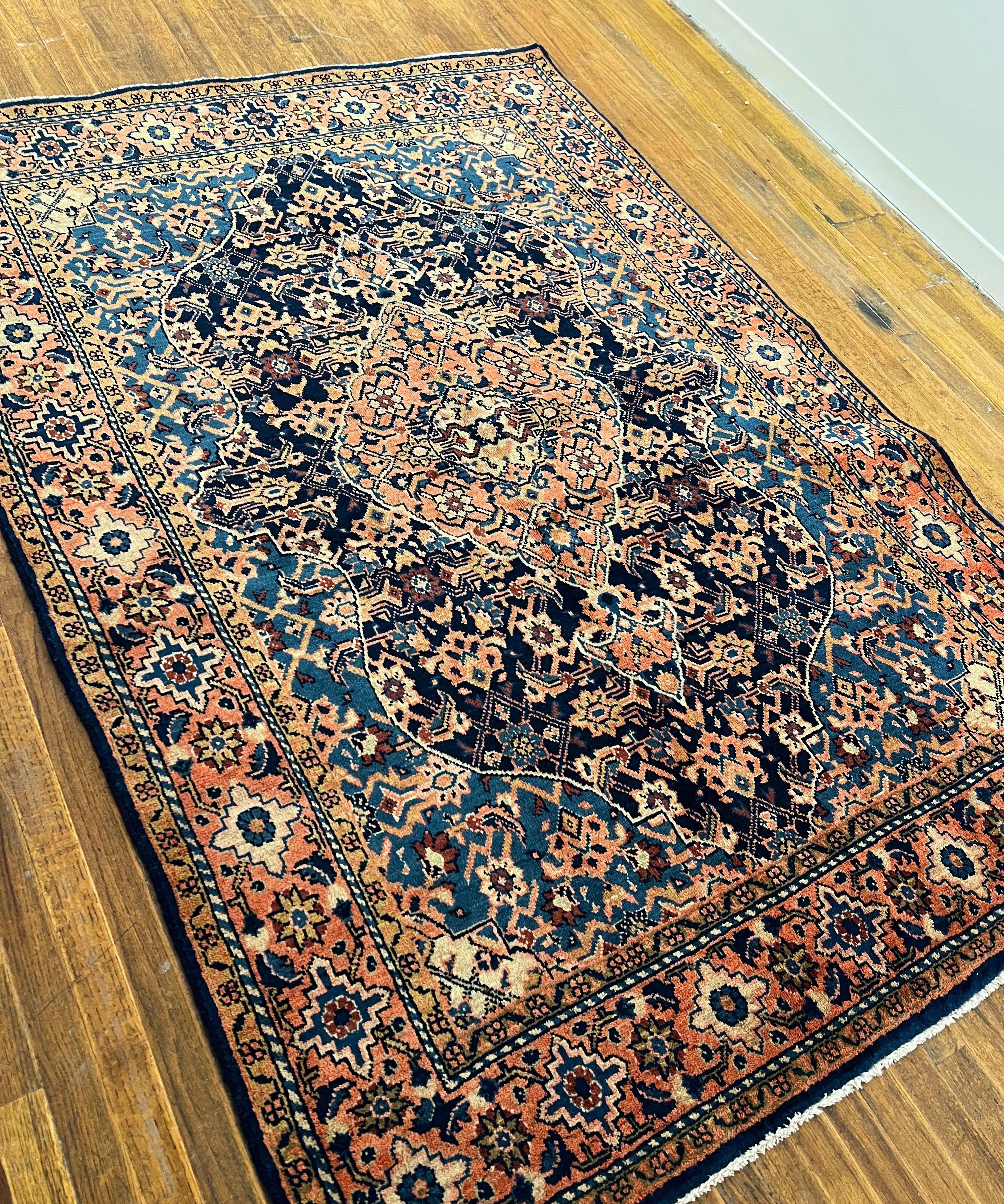 Persian-style area rug laid diagonally, dark navy center medallion with rust and teal details.