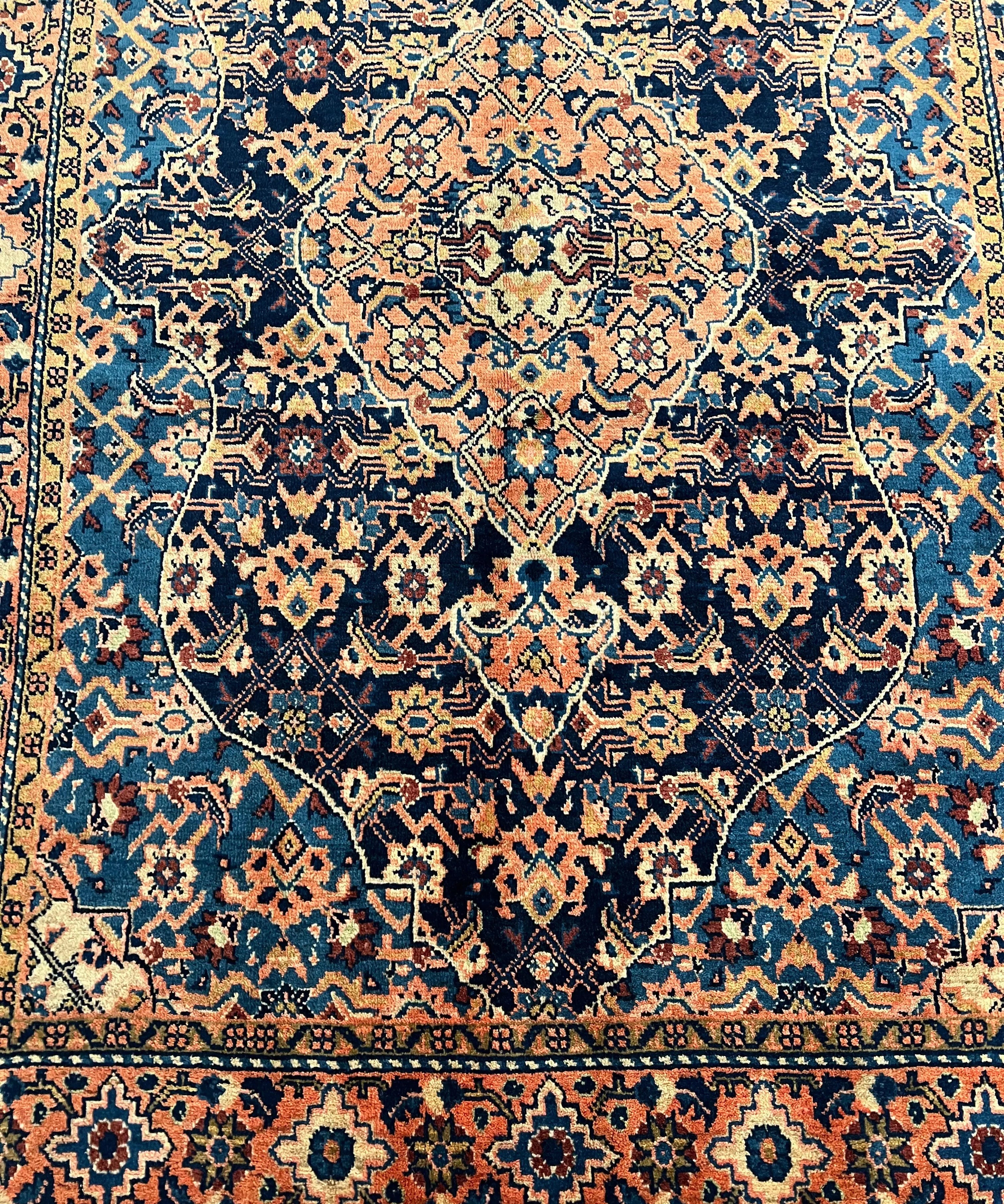 Persian-style rug pattern view: dark blue field with peach, teal, rust, and navy diamonds.