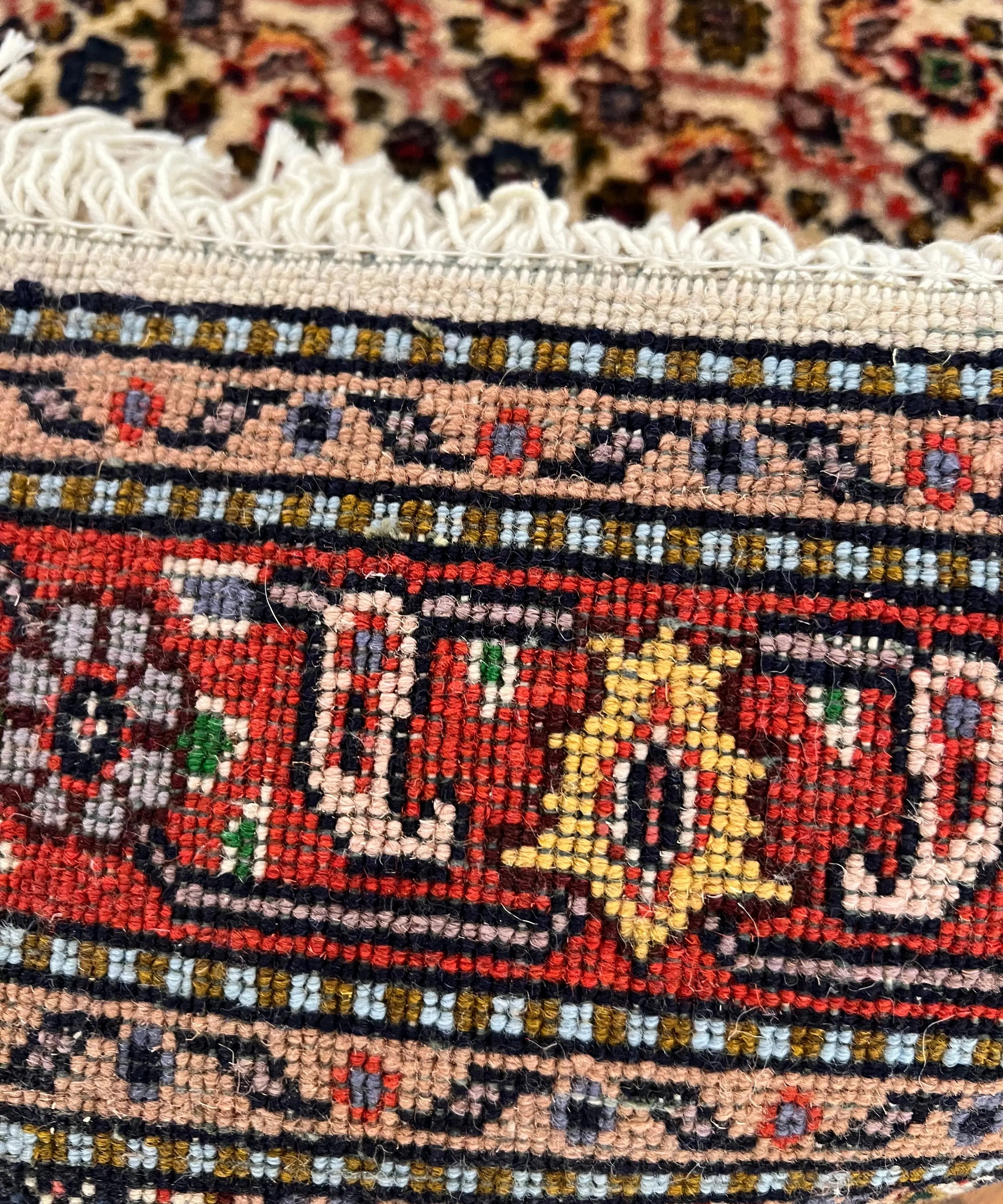 Geometric rug border close-up with red, navy, and cream rows and cream fringe